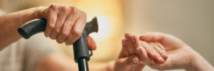 Caregiver gently holding an elderly person’s hand with a walking stick, representing Care247’s compassionate elder care and home healthcare support.